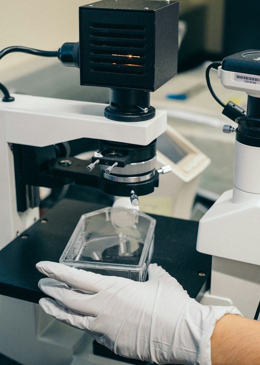 Gloved hands placing a sample under a laboratory microscope