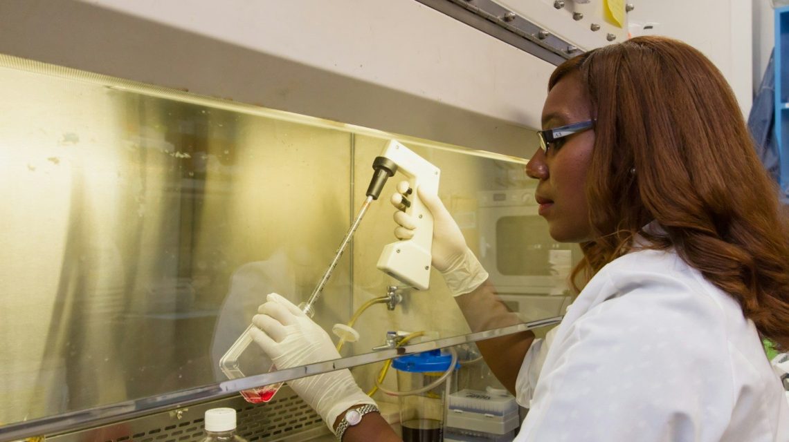 a woman in white lab coat and gloves working on a machine