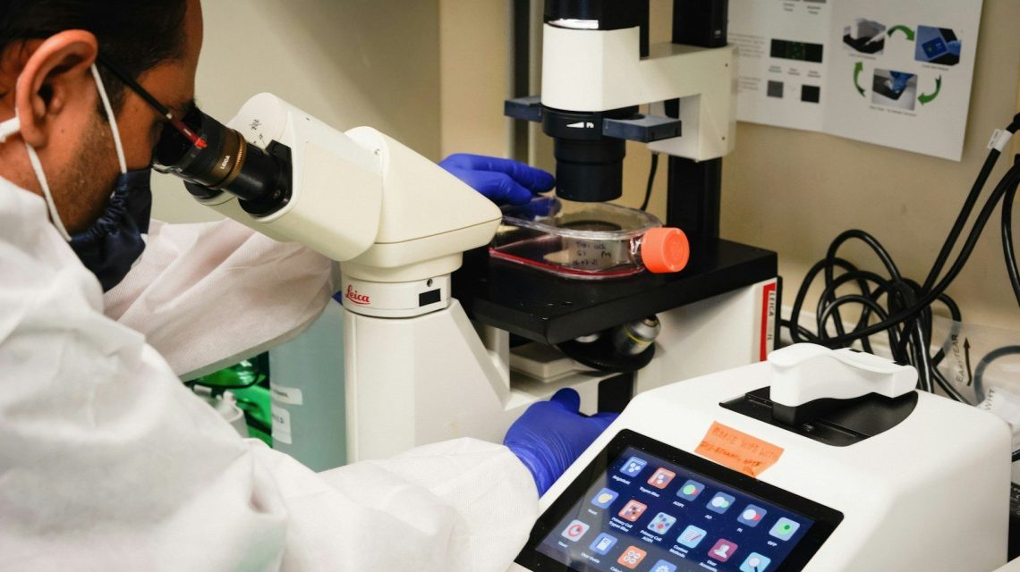 a man in white lab coat looking through a microscope