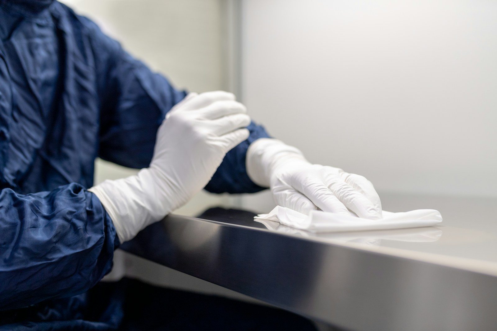 A person in a blue gown and white gloves wiping a metal surface