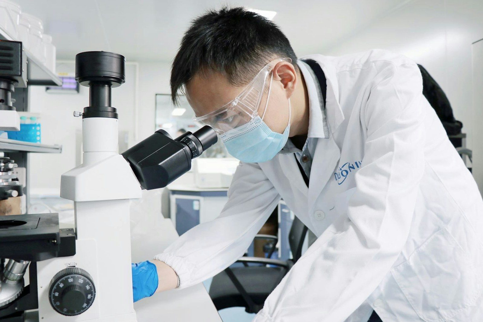 A man in a lab coat and goggles looking through a microscope