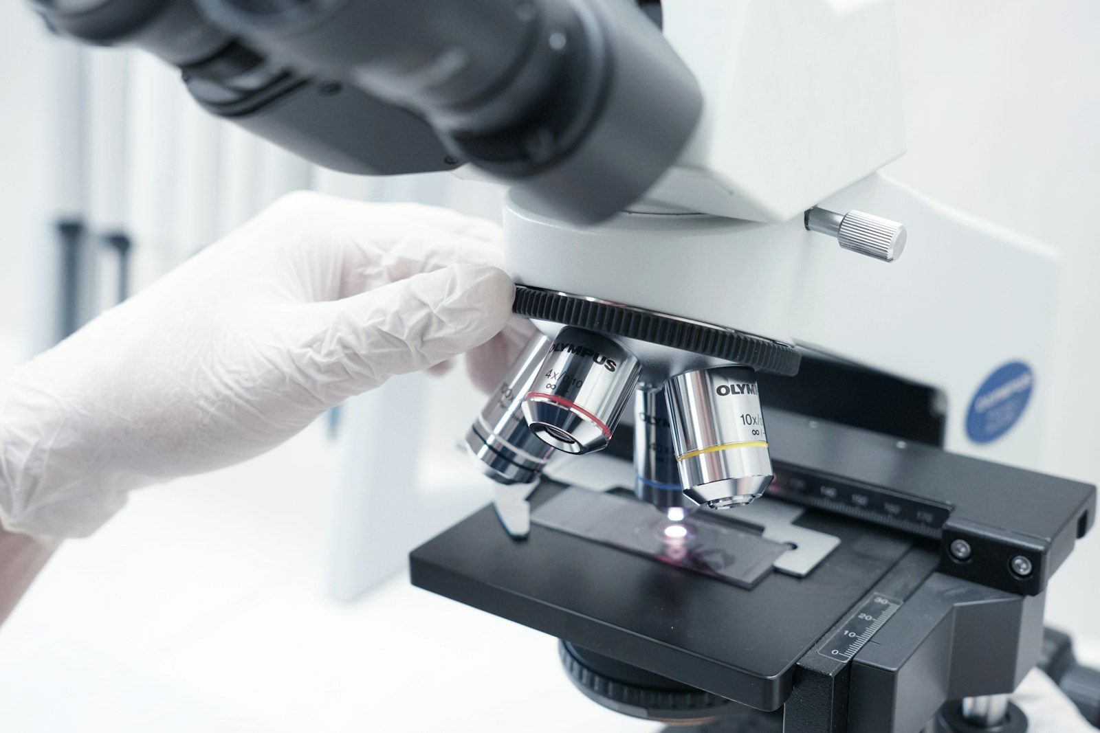 A person in white gloves looking through a microscope