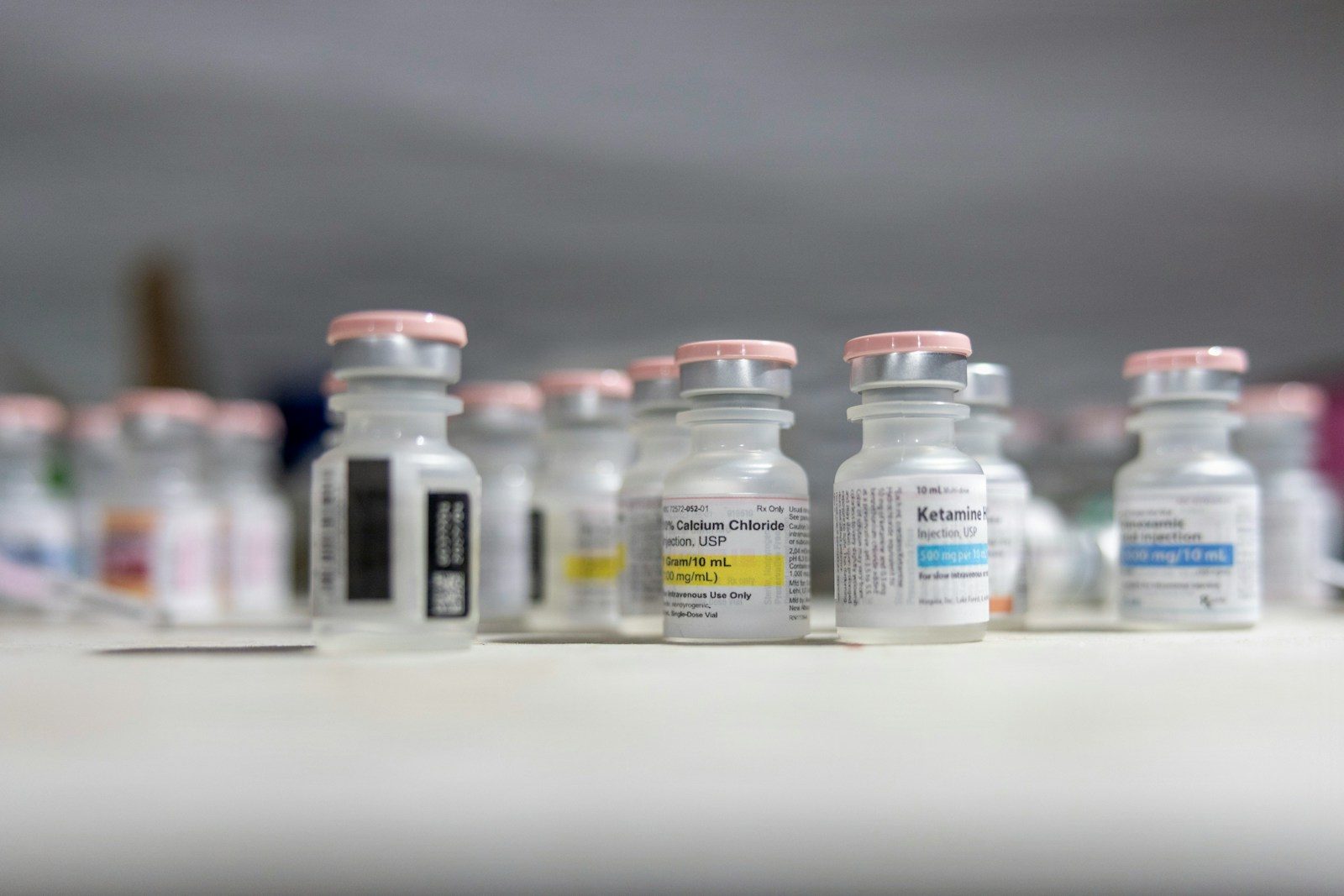 A group of small glass medical vials with pink caps on a surface