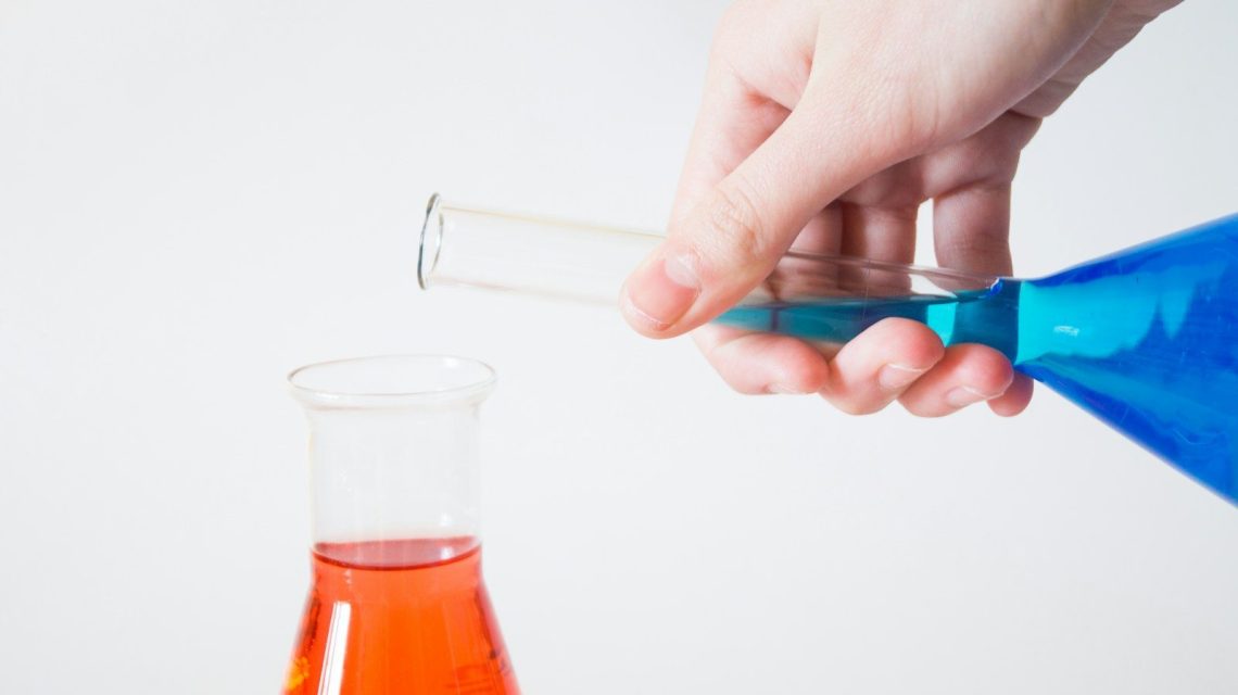 person holding flask pouring to other flask