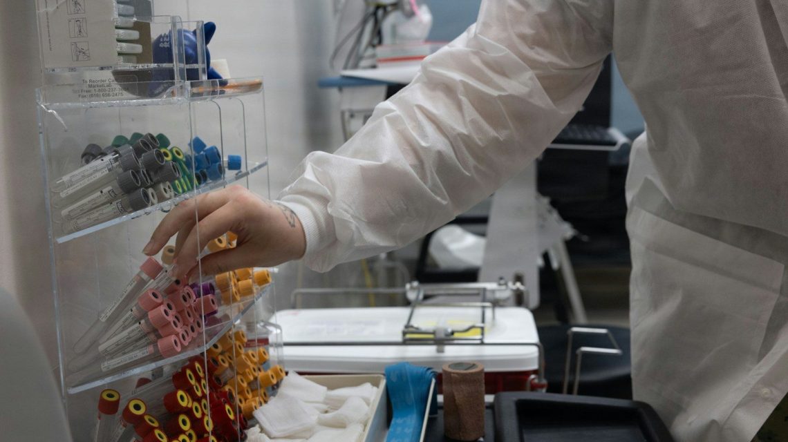 Person in lab coat selecting supplies from rack